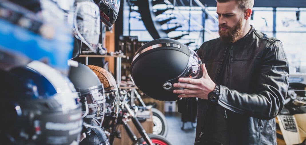 image of a man holding a motorcycle helmet in a bike shop - learn how much you should pay for a good motorcycle helmet with Motohorse, a motorcycle & powersports parts and accessories shop